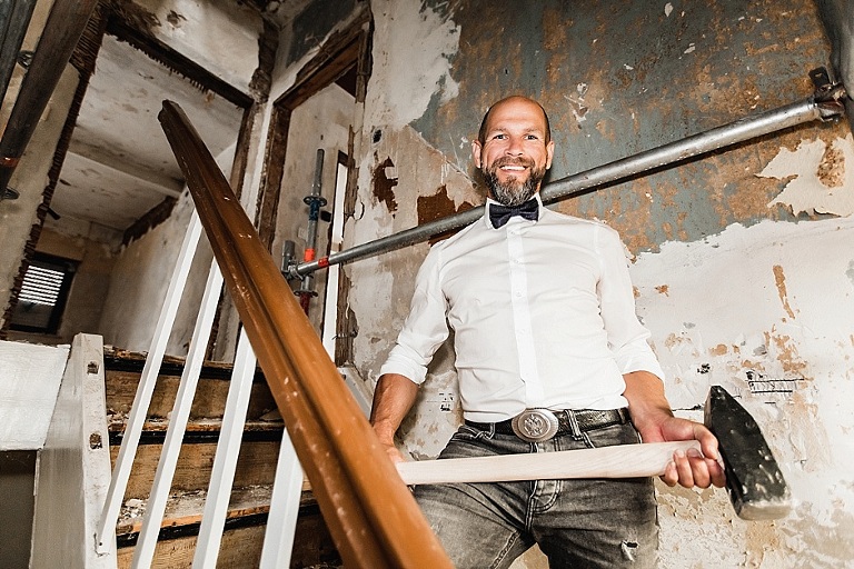 Mann mit Hammer in der Hand steht auf der Treppe eines sanierungsbedürftigen Hauses. Imagebilder, Bilder für website, corporate Photography, Imagebilder, Werbefotografie, Homepagebilder, Businessfotografie